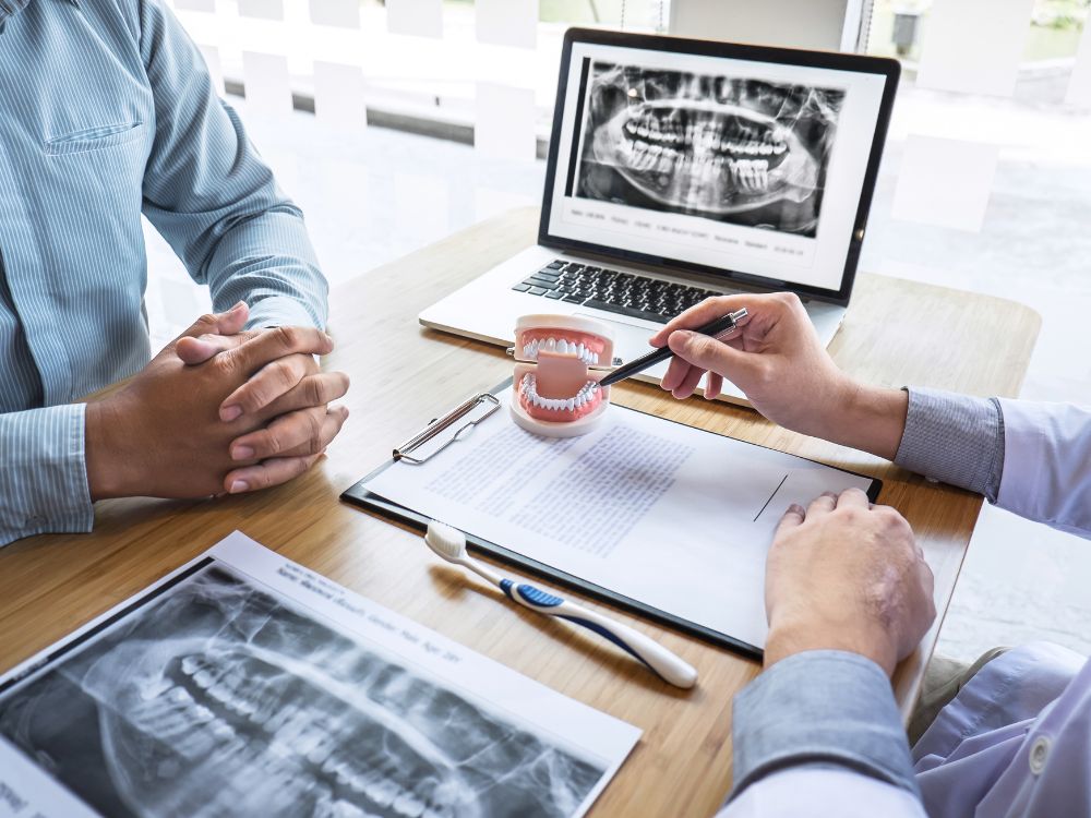 Dentista explicando procedimento com modelo odontológico e radiografia, ilustrando o que é implante zigomático em consulta clínica.