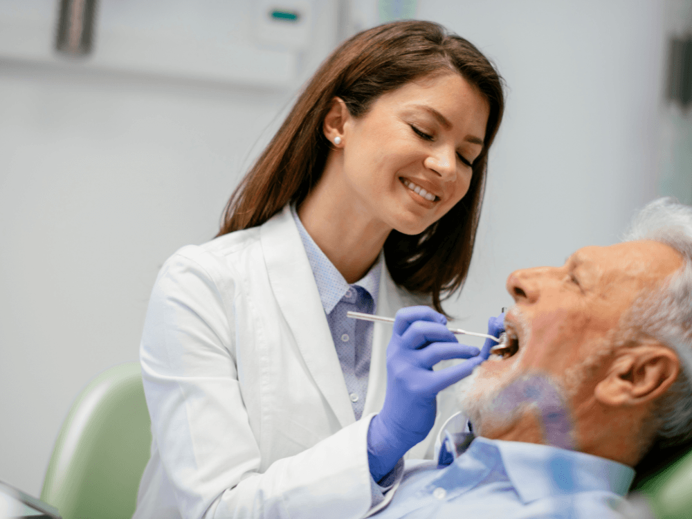 Dentista examina a boca de um homem idoso reclinado na cadeira durante consulta para avaliação do tratamento com implante dentário.