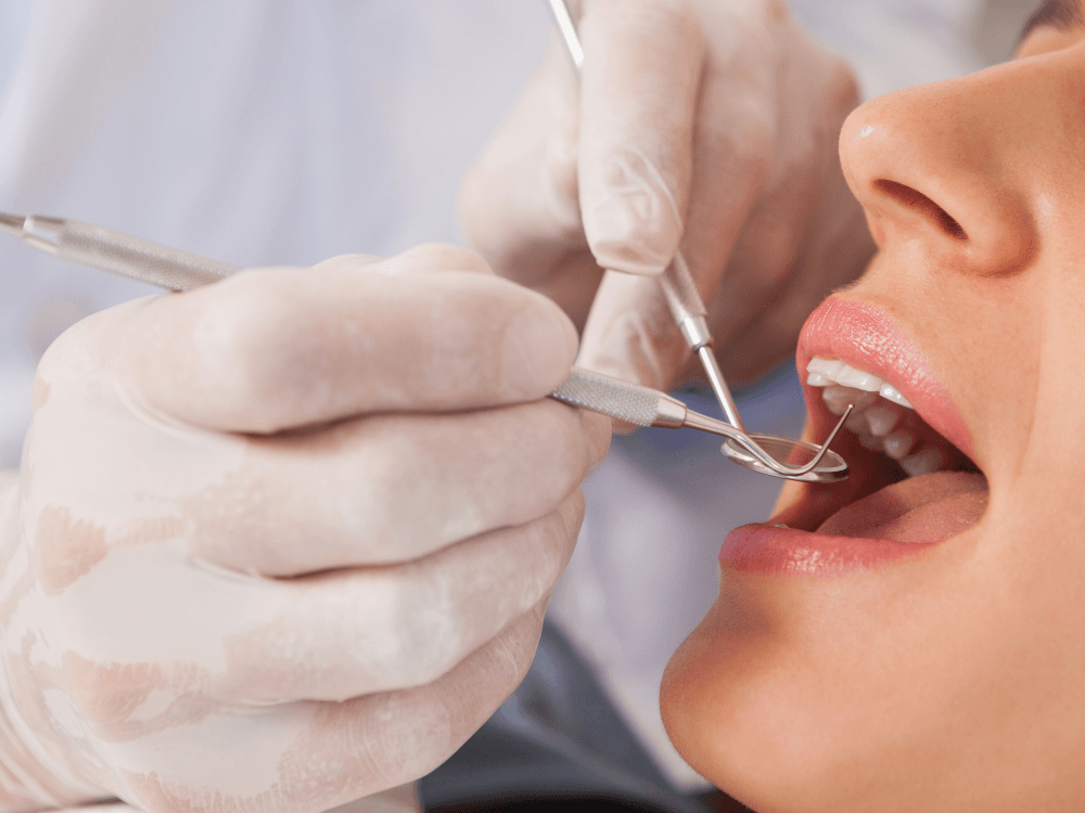 Dentista examina os dentes de uma paciente com espelho e sonda odontológica durante consulta de avaliação para implante dentário.